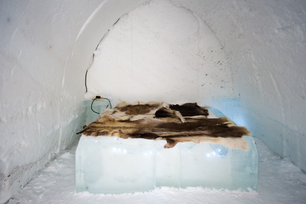 The interior of an igloo with a bed made of ice and covered with animal skins